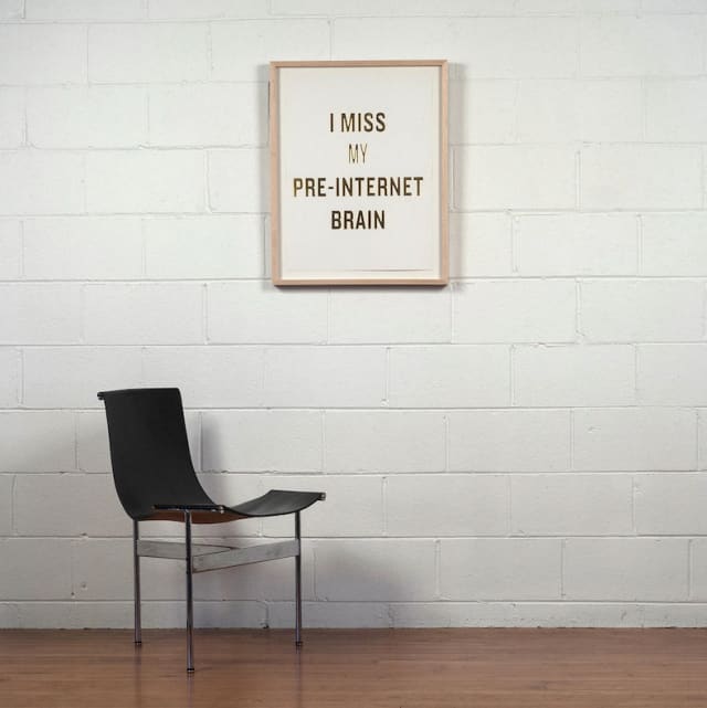 A white framed canvas on a wall that says "I miss my pre-internet brain" with a chair in front of it.