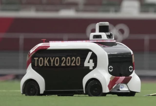 A photo of a little autonomous vehicle with "Tokyo 2020" on the side. It's not clear what it's doing in this photo but it's pretty cute.